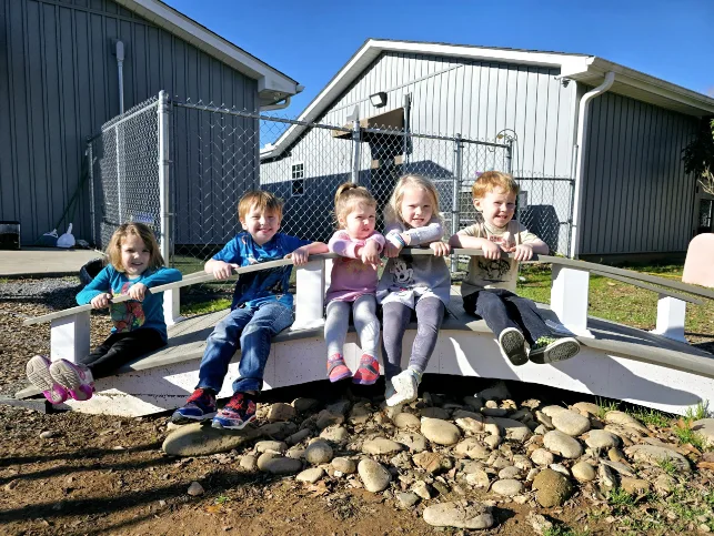 A group of children from a daycare center happily sitting on a bridge, enjoying a sunny day together in Landrum, SC
