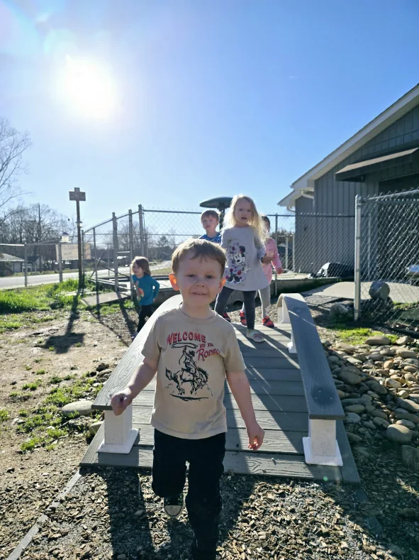 Children from a daycare center joyfully crossing a wooden bridge, exploring their surroundings together in Landrum, SC